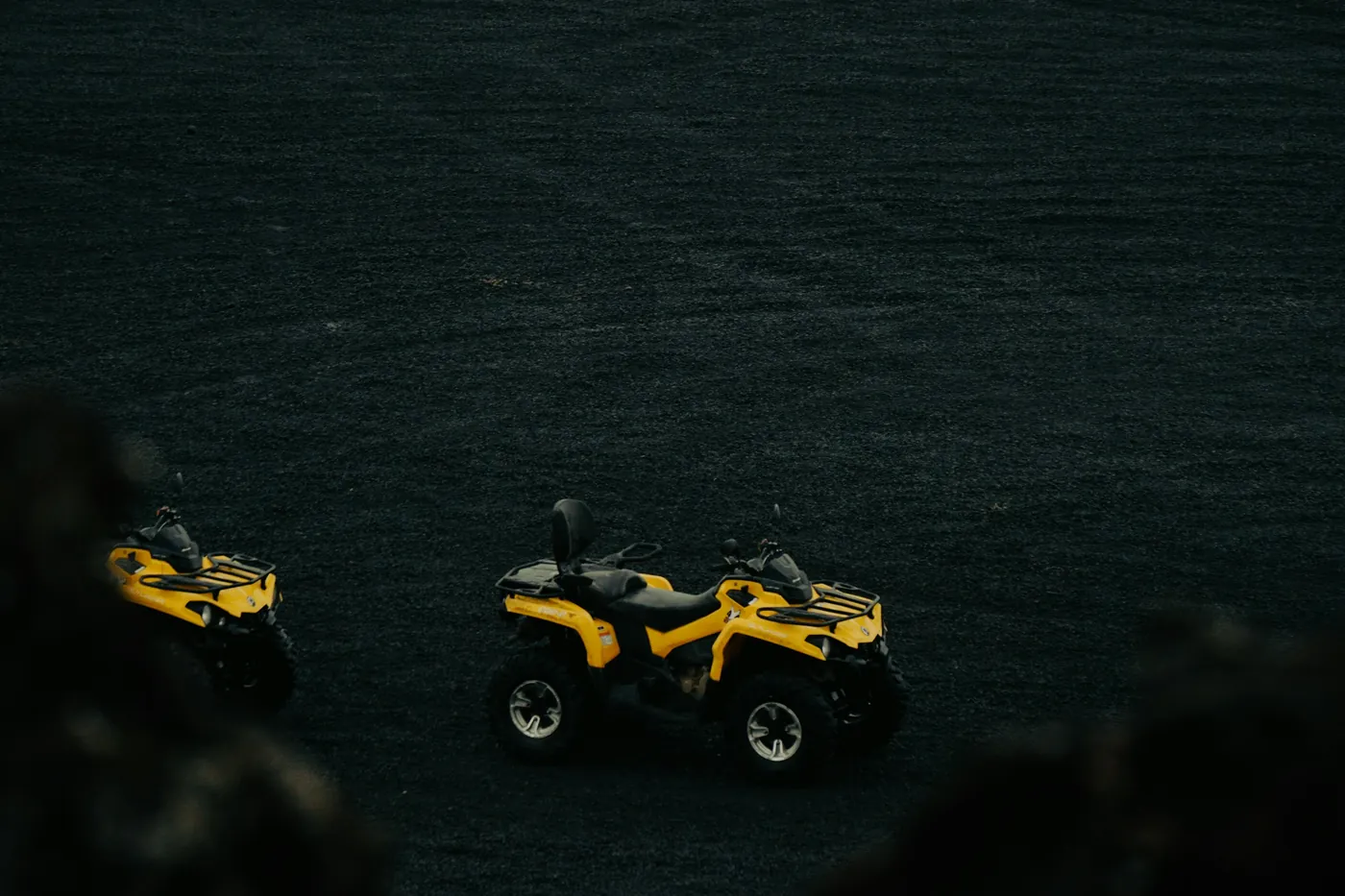 Two yellow quad bikes parked on a wide dark volcanic sand plain