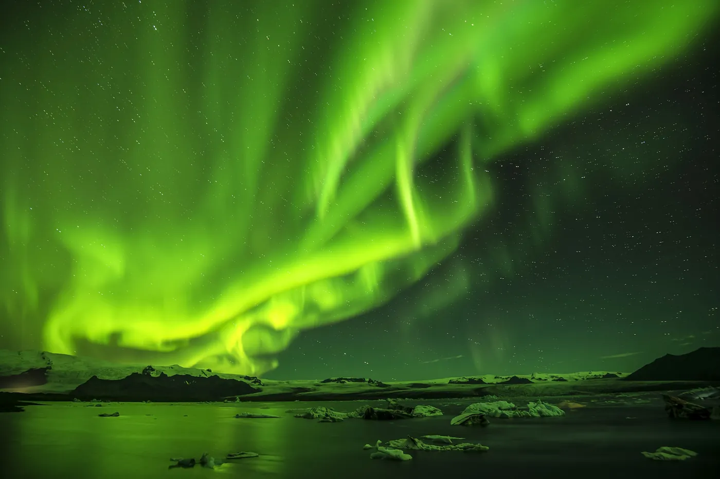Bright green northern lights above a dark glacial lagoon with floating ice