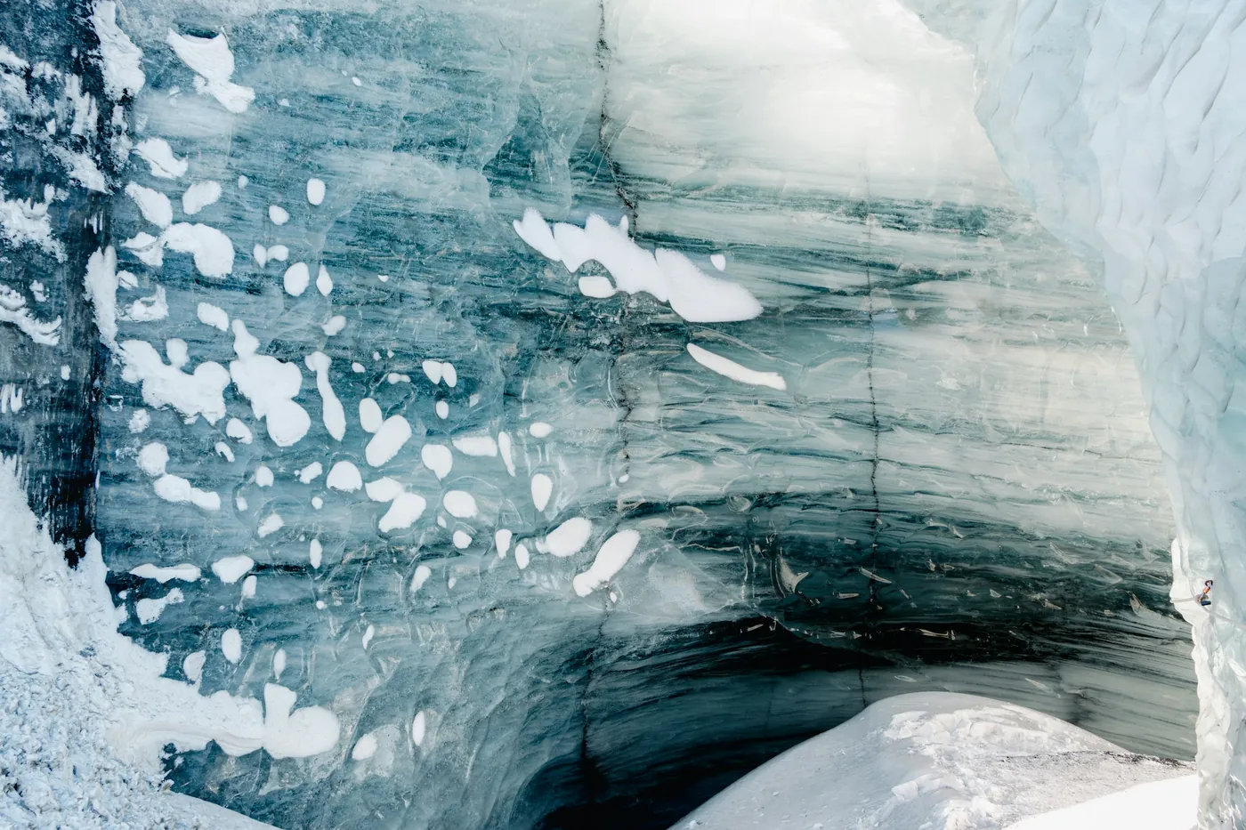 Wall of blue glacier ice streaked with dark ash layers inside an ice cave