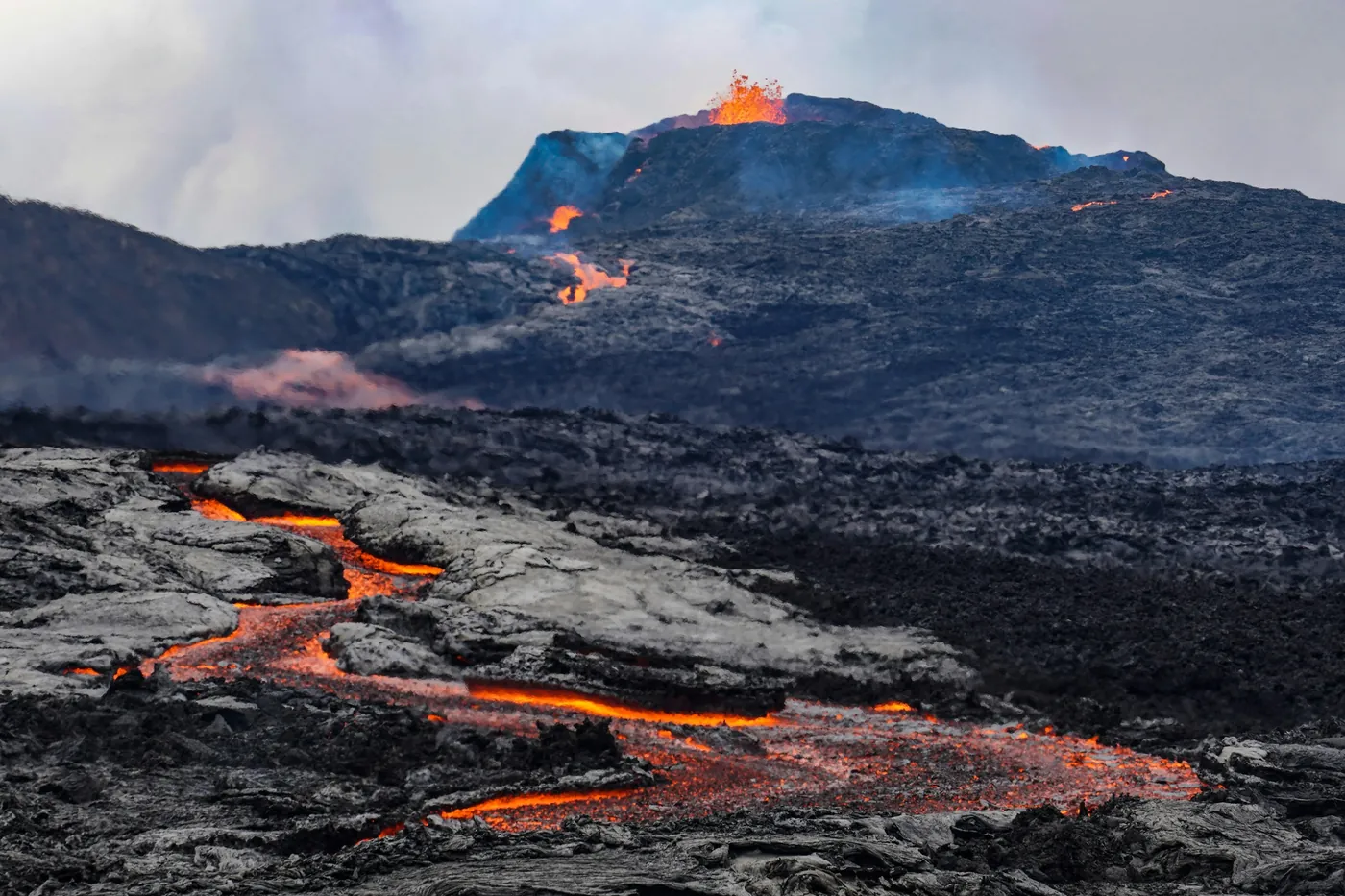 Lava naranja incandescente que fluye sobre lava oscura enfriada bajo un cráter en erupción