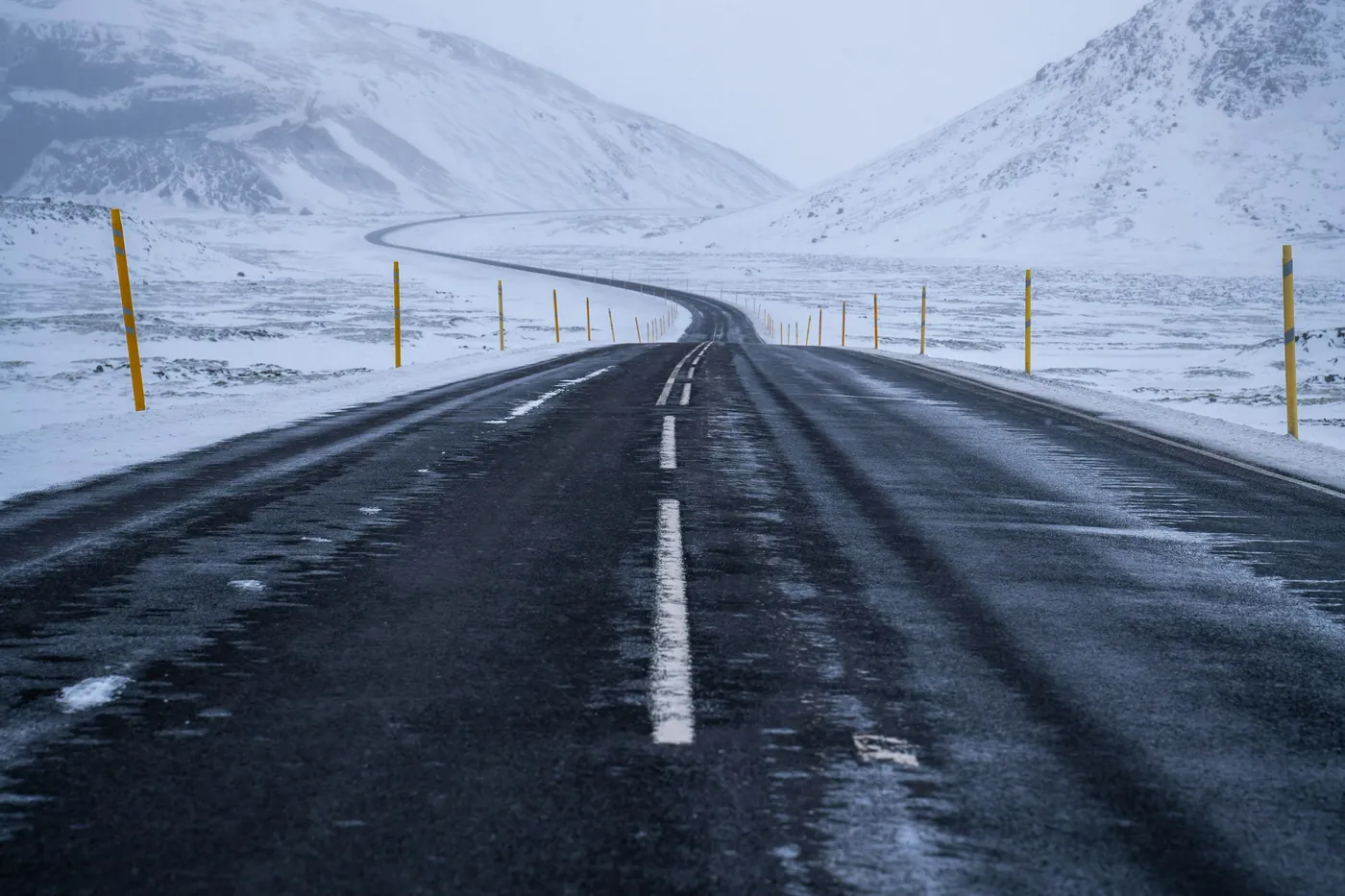Strada ghiacciata a due corsie con paletti gialli che curva tra colline coperte di neve