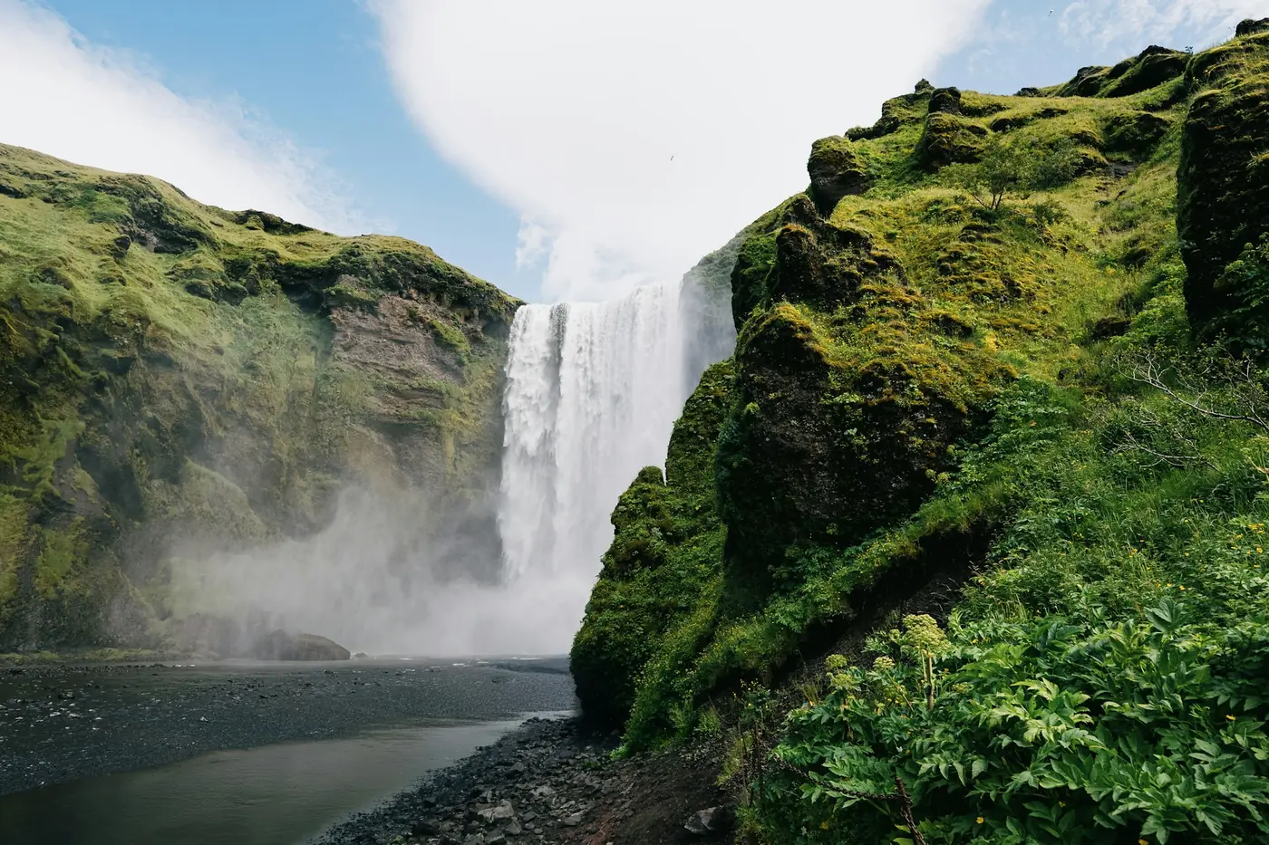 Tall waterfall framed by steep green mossy cliffs, spray drifting over the river